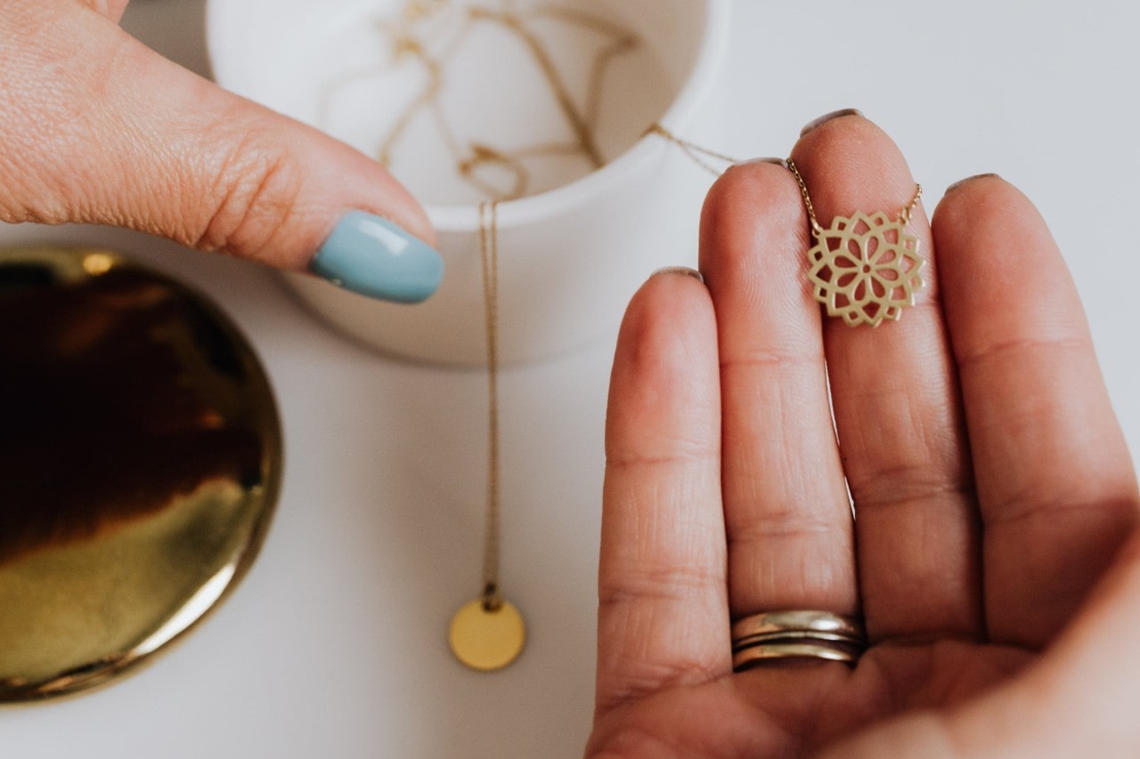a person’s hand holding a yellow gold necklace with a mandala motif pendant