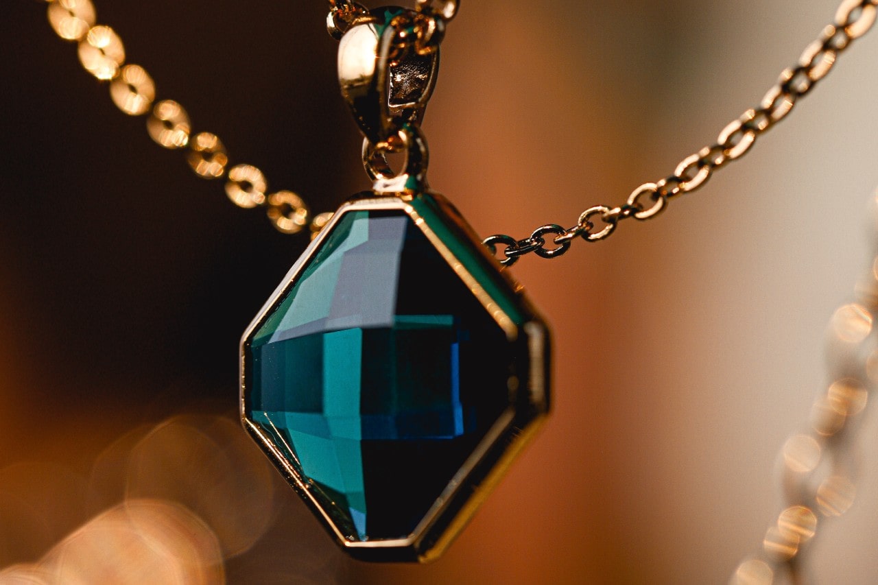 a yellow gold necklace featuring a deep teal pendant cut into a geometric shape