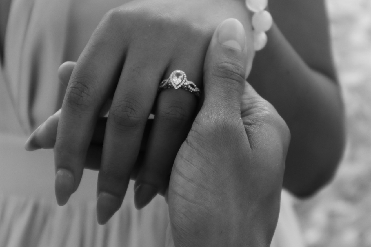 A man holds his bride’s hand, inspecting her pear shaped halo engagement ring.