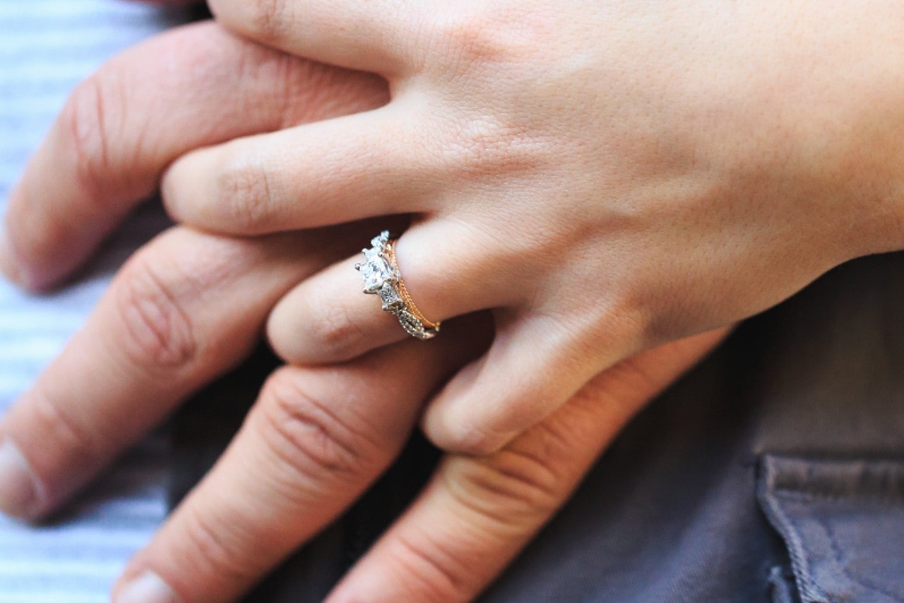 a couple’s hands intertwined, the woman’s hand wearing a three stone engagement ring
