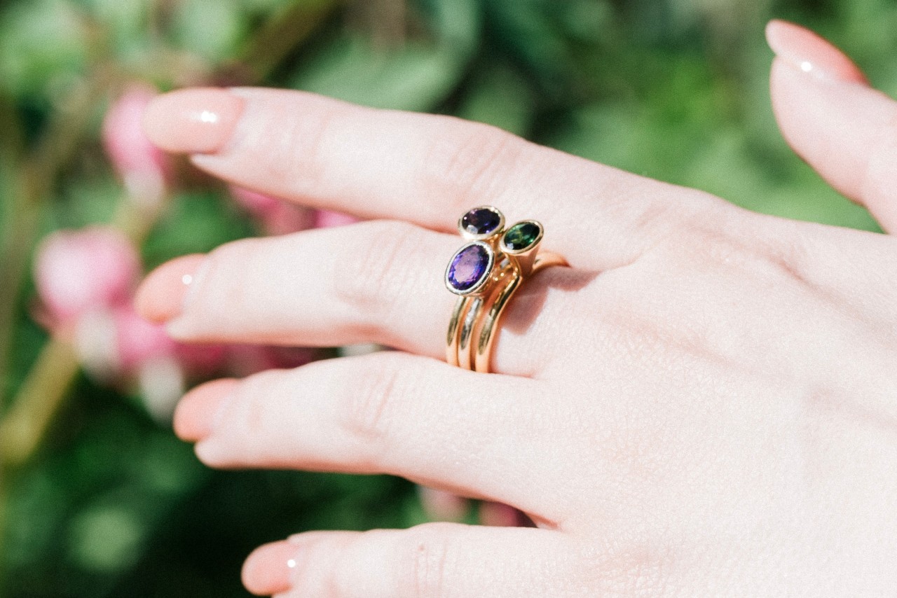 close up image of a woman’s hand wearing a stack of three gemstone fashion rings