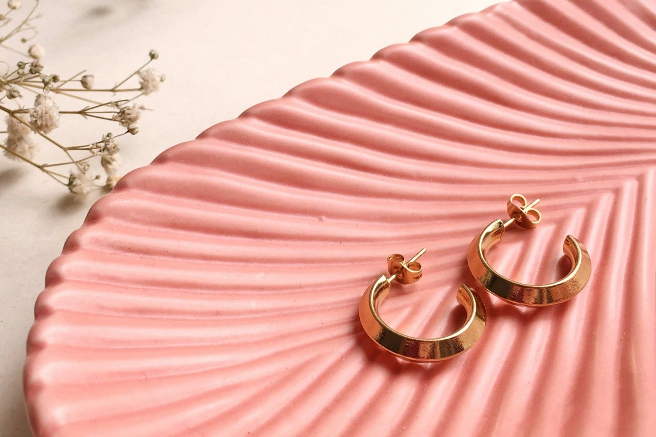 a pair of yellow gold huggies sitting in a pink textured dish