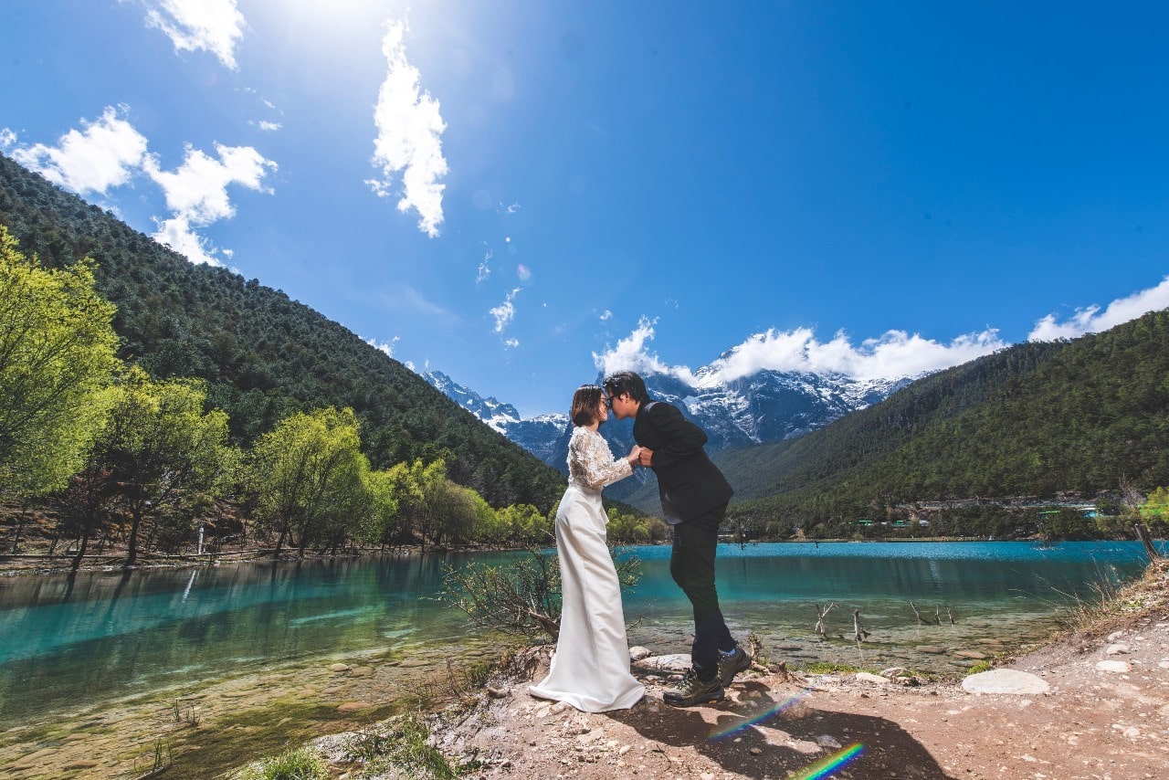 a couple embracing by a body of water and mountains