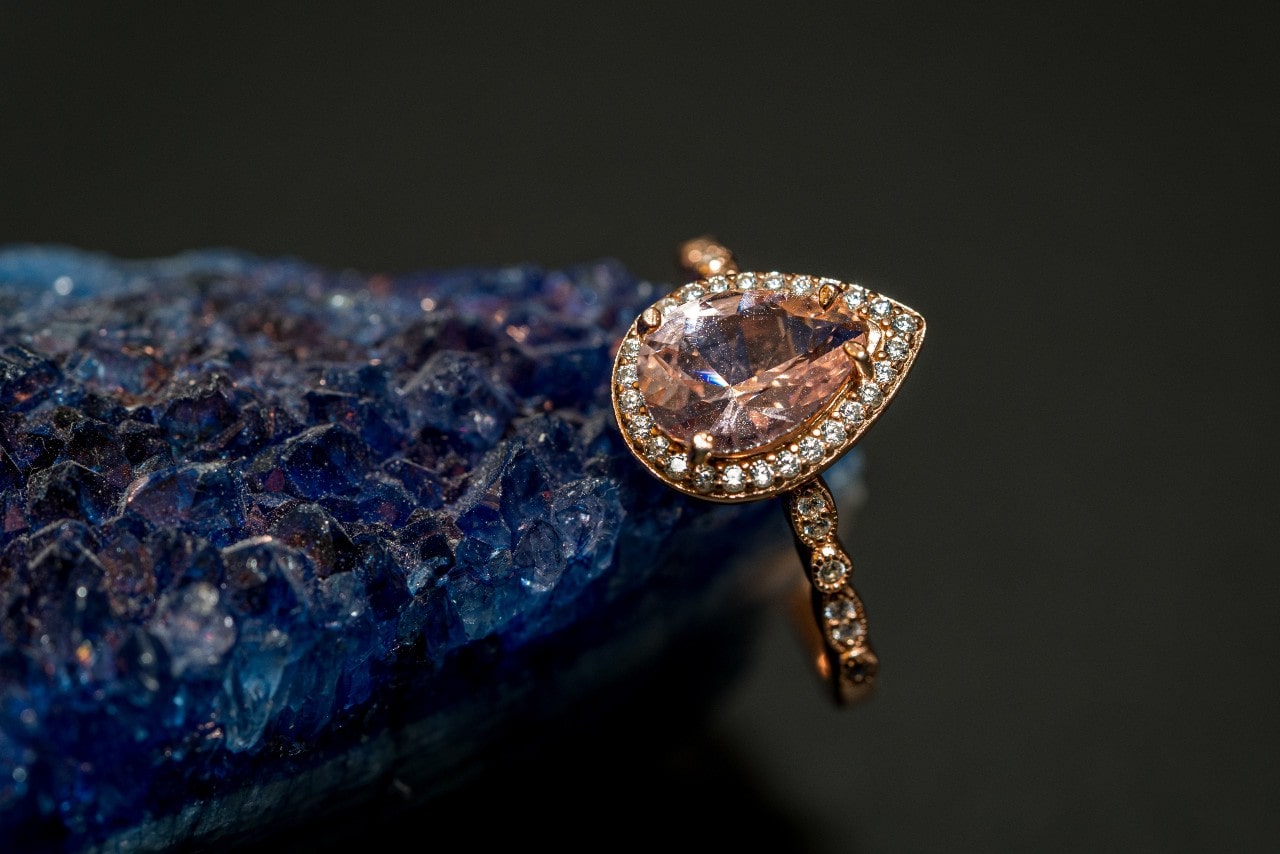 a rose gold ring with a pink pear shaped gemstone resting on a blue crystal