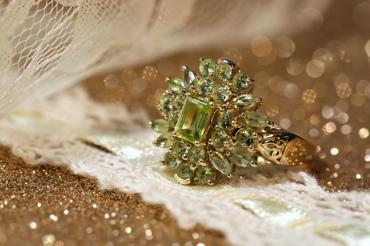 a peridot cocktail ring sitting on a glittering surface covered in a strip of lace