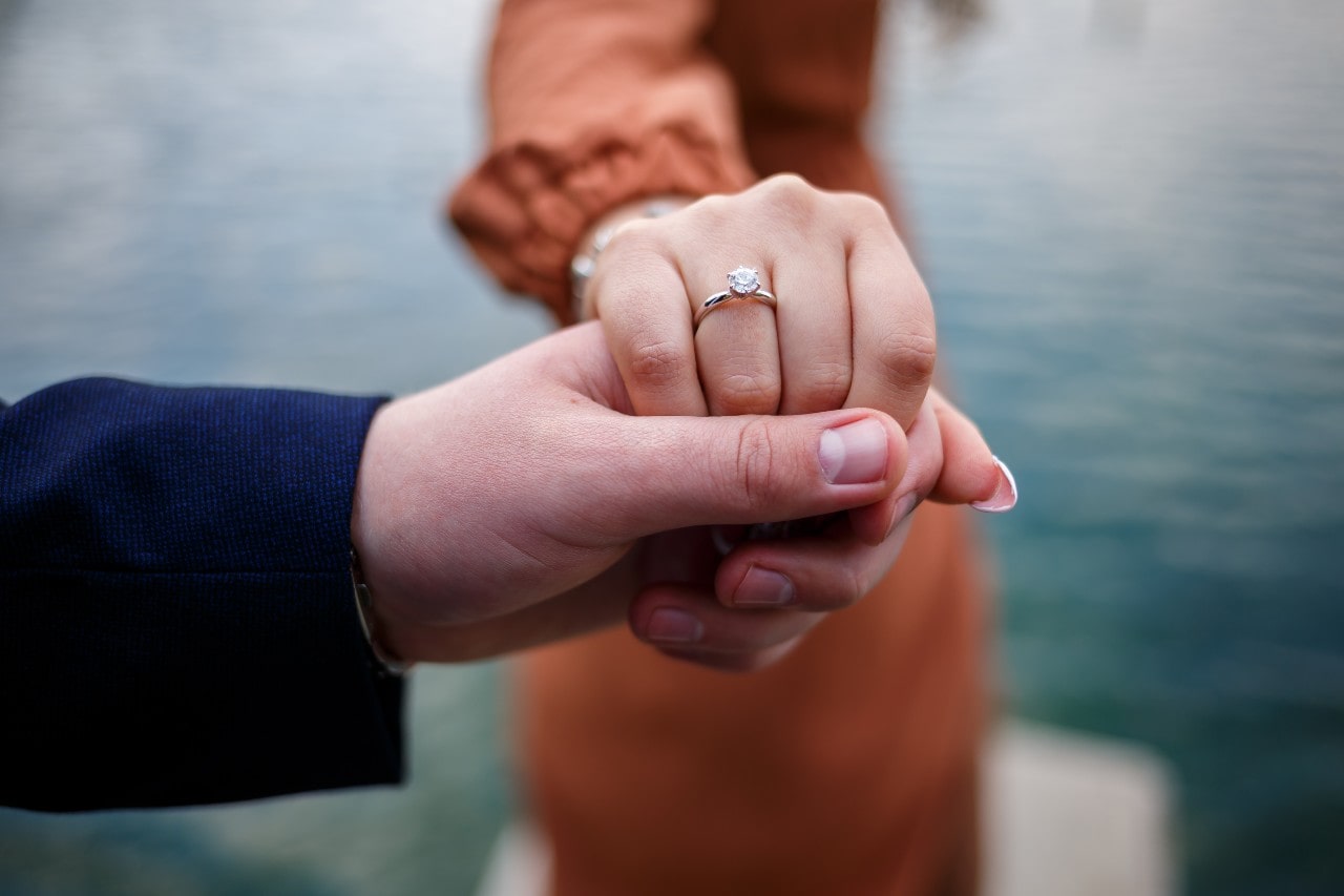 Woman wearing a diamond ring and holding a man’s hand. 