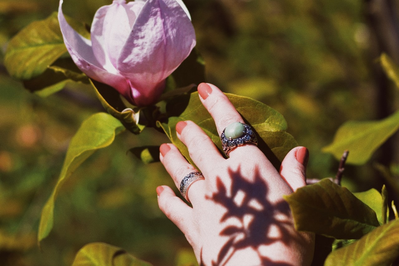 a hand reaching toward a purple flower and wearing silver cocktail rings