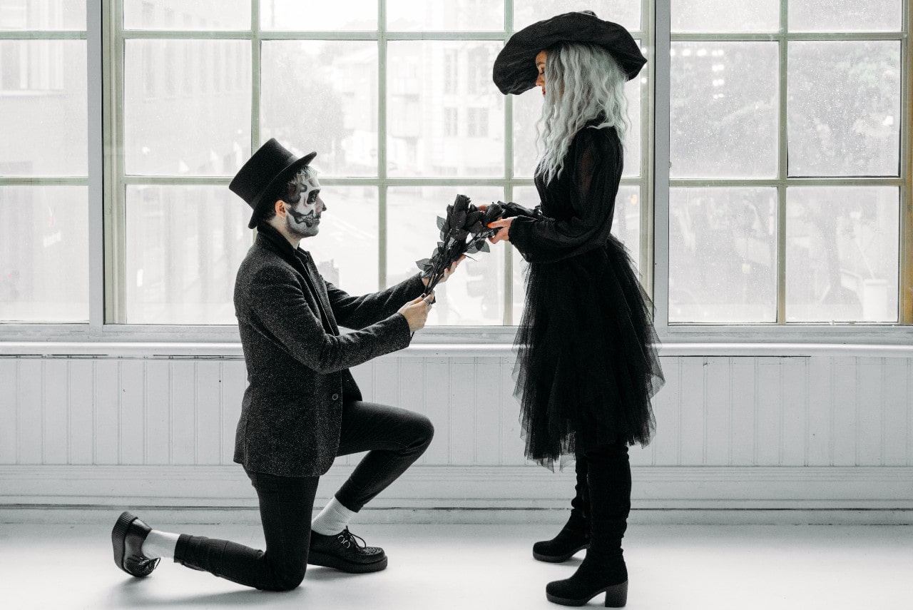 A man dressed as a skeleton proposes to a woman dressed as a witch.