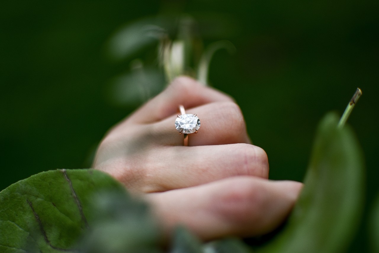 a person’s hand holding a bouquet and wearing an oval-cut engagement ring