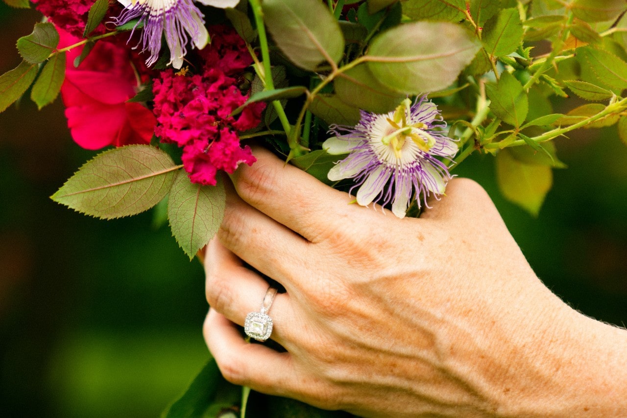 a woman’s hand holding a bouquet of flowers and wearing a white gold engagement ring