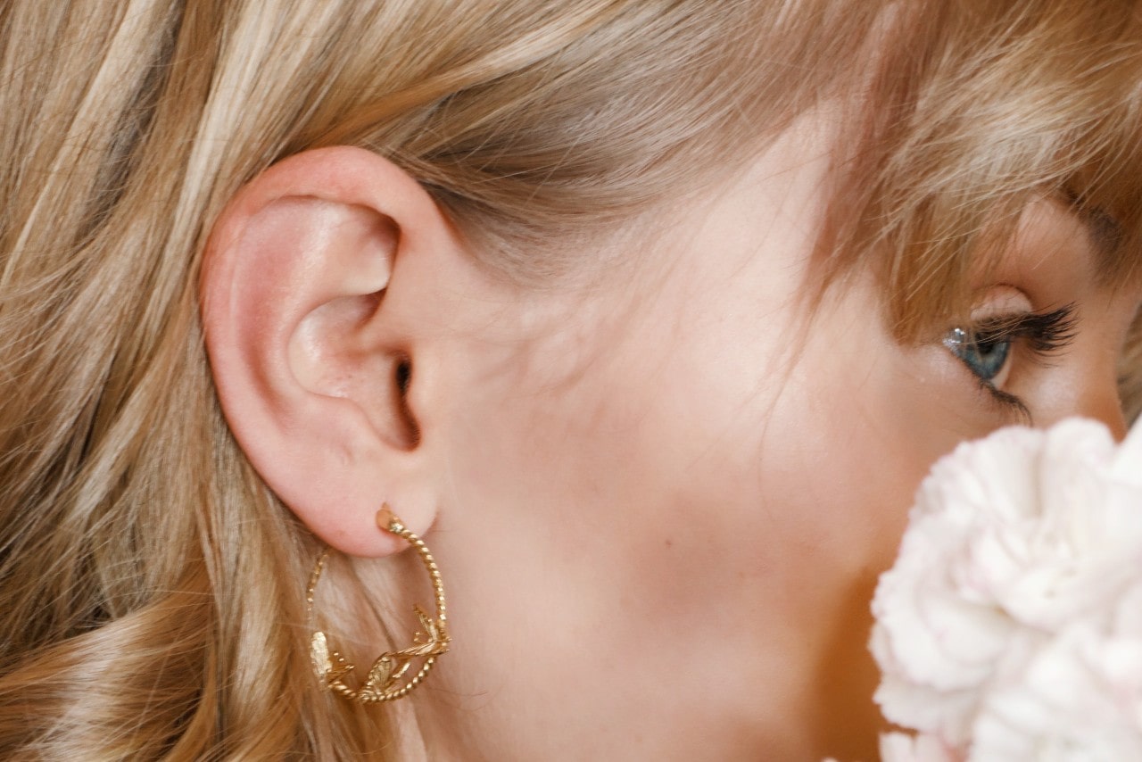 close up image of a woman wearing gold hoops and looking away from the camera