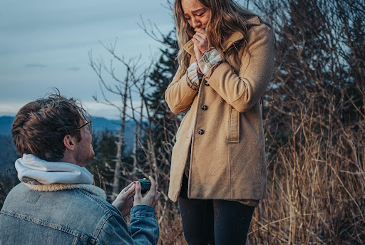 A man down on one knee proposing to a woman on a mountain