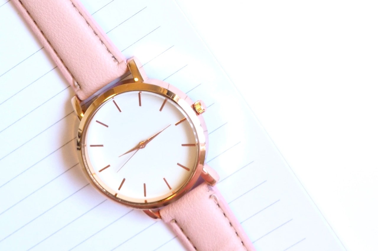Pink women’s watch sitting on a notebook.