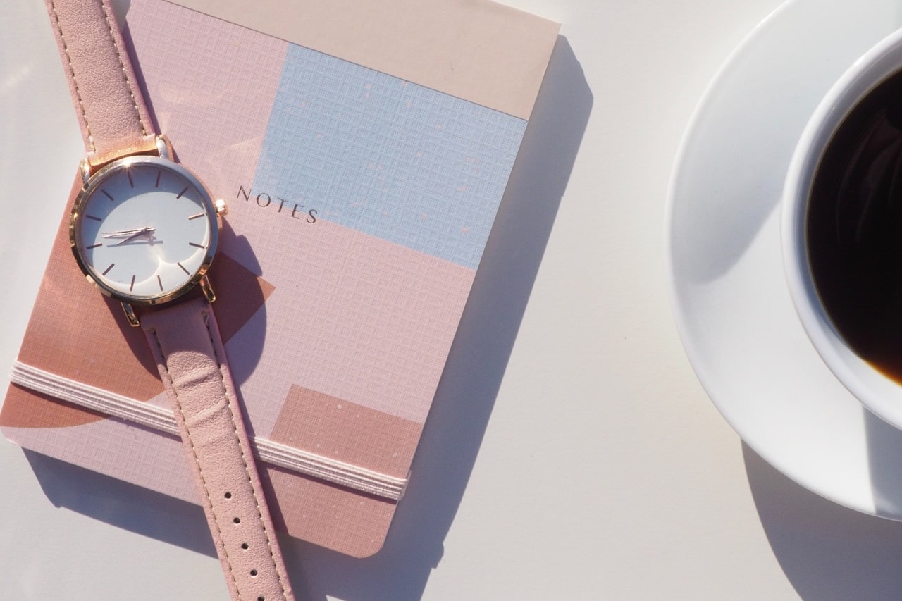 Sleek minimalist women’s watch with pink strap next to a cup of black coffee.