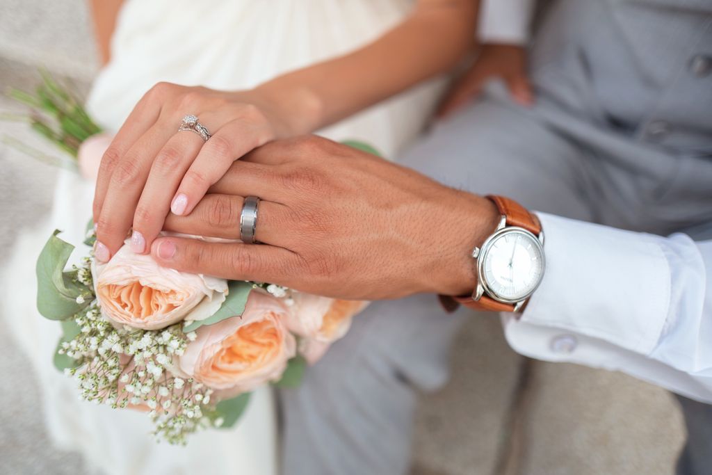 Newlyweds holding hands, one of which dons a men’s wedding band.