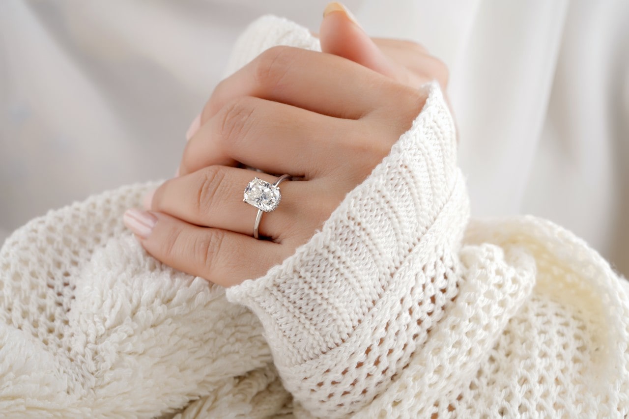 a woman cuddled in a sweater wears a platinum solitaire ring with an oval cut diamond.
