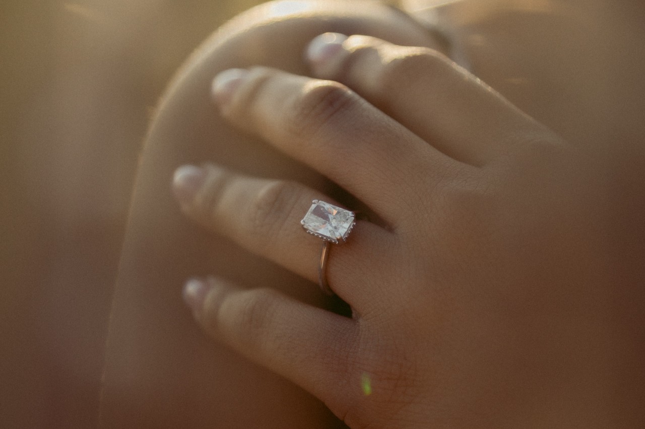a woman’s hand resting on her shoulder and wearing a solitaire engagement ring