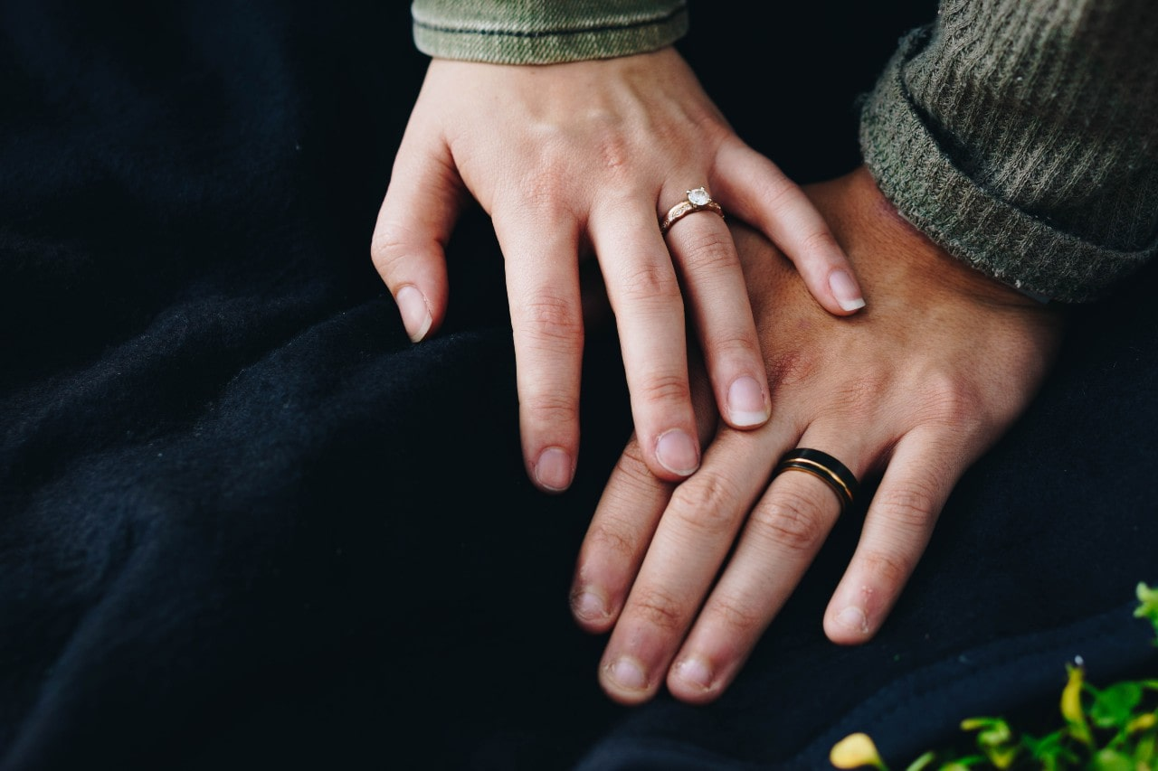 A married couple holds hands while showing off their wedding bands.